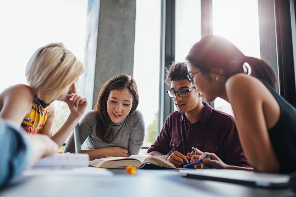 Four students hunched over a textbook discussing an assignment
